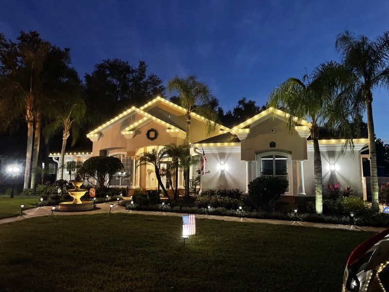 Home with roofline lights, lit wreaths on windows and a lit entryway at twilight