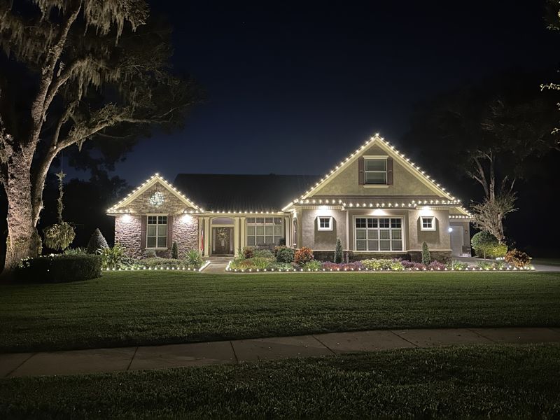 Ranch-style home with warm white roofline lighting and lit landscape beds